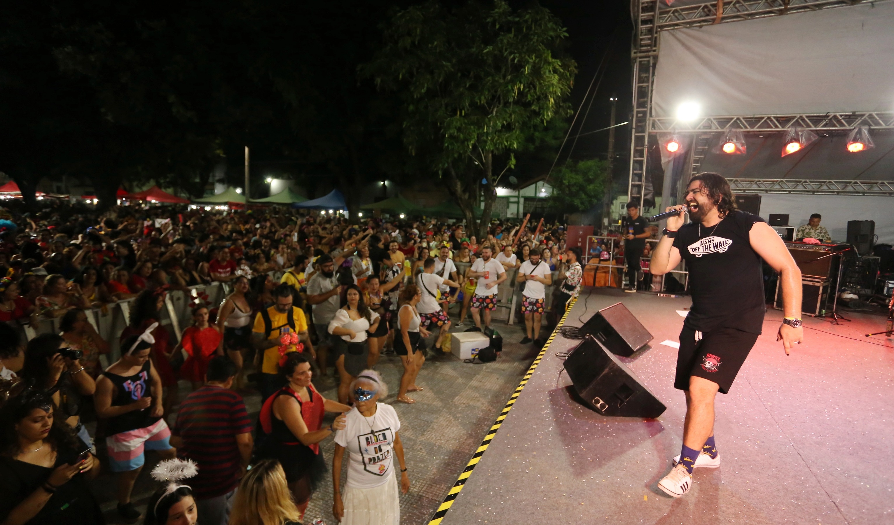 banda alfazemas tocando em palco, cantor pulando e público em frente assistindo na praça